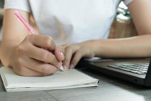 jeune femme d'affaires assise à table avec un ordinateur portable et prenant des notes dans un cahier. photo