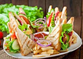 sandwich club avec fromage, concombre, tomate, viande fumée et salami. servi avec frites.