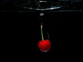 Red sweet cherry sous l'eau isolé sur fond noir photo