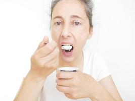 femme de quarante neuf ans dans un t-shirt blanc sur fond blanc mangeant un yaourt photo