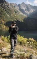 photographe de jeune homme prenant des photos avec un appareil photo numérique dans une montagne.