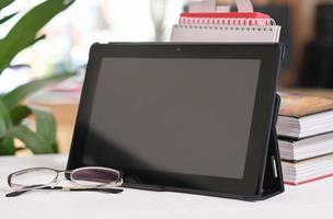 tablette numérique sur un bureau avec des lunettes et des livres dans un salon. éducation, apprentissage à domicile, concept d'étude en ligne. photo