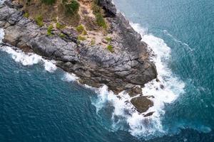 vue aérienne drone caméra de haut en bas des rochers du bord de mer dans un océan bleu surface de la mer turquoise des vagues de mer étonnantes se brisant sur le paysage marin des rochers. image de haute qualité des vagues de la mer à phuket en thaïlande photo