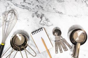 concept d'outils de cuisine sur table en marbre. mesurer les ingrédients en suivant la recette avec des tasses à mesurer, des cuillères à mesurer et battre avec un fouet. photo