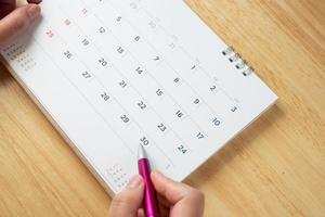 page de calendrier avec une main féminine tenant un stylo sur la table du bureau photo