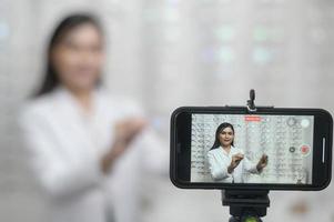 jeune ophtalmologiste faisant du streaming en direct via un smartphone présente une nouvelle collection de lunettes dans un centre optique, concept de soins oculaires. photo