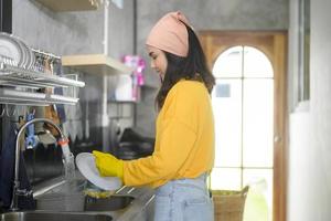 jeune femme heureuse portant des gants jaunes faisant la vaisselle dans la cuisine à la maison