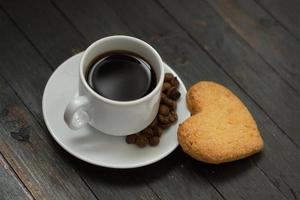 une tasse de café avec des grains de café et un biscuit d'amour sur une surface en bois.vacances de la saint-valentin photo