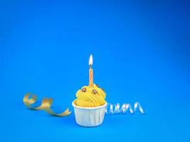 cupcake jaune vif doux avec bougie arc sur fond bleu avec espace de copie. bonne fête d'anniversaire photo