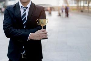 homme d'affaires, tenant une coupe du trophée d'or est vainqueur d'un concours avec fond de ville. notion de victoire. photo