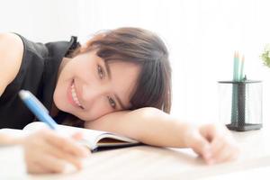 beau portrait jeune femme asiatique sourire et bonne écriture examen d'apprentissage ou devoirs et couché avec bureau, mode de vie beauté asie fille avec travail, éducation et concept d'entreprise. photo