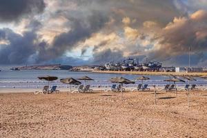 Chaises de plage avec parasols en rangée sur une plage de sable en journée ensoleillée contre ciel nuageux photo