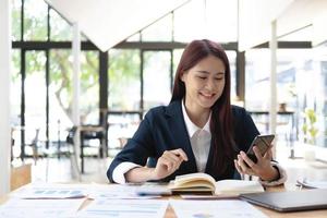 femme asiatique parlant au téléphone et travaillant sur un ordinateur portable avec un visage souriant, conversations professionnelles sur téléphone portable, travail au café, style de vie au café, séjour au café, nouvelle normalité, apprentissage, distanciation sociale. photo