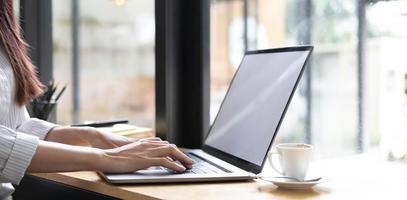 la main d'une femme d'affaires tape un clavier sur un ordinateur portable avec un écran blanc vierge. gros plan des mains de femme travaillant sur le bureau. photo