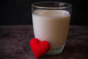 un verre de lait froid et une petite forme de coeur avec un fond de mur sombre. concept de soins de santé. photo