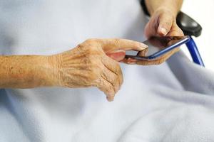 une vieille dame asiatique âgée ou âgée utilise ou joue des téléphones portables, tout en étant assise dans un fauteuil roulant. concept de soins de santé, médical et technologique. photo