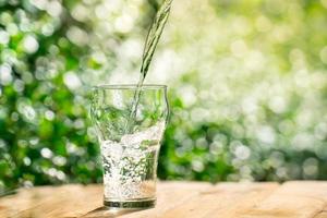 verser de l'eau d'une bouteille en plastique dans un verre. l'arrière-plan des plantes du jardin. mise au point douce. photo