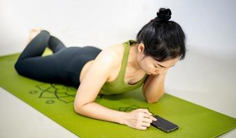 femmes jouant au mobile et assises sur le tapis de yoga vert tout en se reposant pour une pratique à la maison. photo