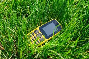 un téléphone mobile obsolète à bouton-poussoir jeté dans une herbe verte dense, polluant la nature photo