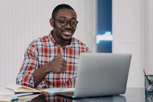 l'homme afro-américain montre comme ou le geste du pouce vers le haut communique en ligne sur un ordinateur portable. commentaire positif photo