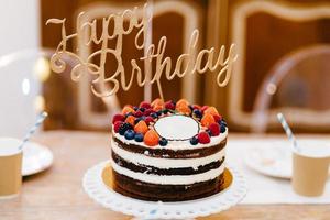 savoureux gâteau décoré pour la fête d'anniversaire debout sur une table en bois. table servie pour l'anniversaire de la célébration. table de vacances avec gâteau. table des desserts. notion de célébration photo