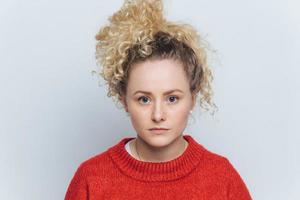 photo de tête d'une belle femme sérieuse et heureuse avec une peau saine, des yeux bleus et des cheveux bouclés, habillée avec désinvolture, isolée sur fond de studio blanc. personnes, expressions faciales et concept de beauté