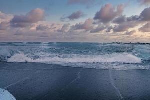 vue panoramique des vagues sur le rivage de sable noir de la plage de diamants contre le ciel au coucher du soleil photo