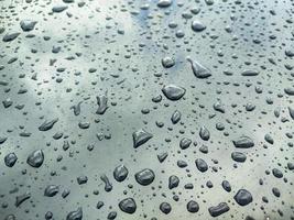 gouttes d'eau sur la surface de la voiture légère recouverte de cire avec réflexion ciel nuageux sur la peinture gris clair photo