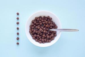 boules de céréales au chocolat dans un bol blanc sur fond bleu. vue de dessus de céréales sèches pour le petit déjeuner. concept pour une alimentation saine photo