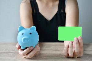 une fille avec une tirelire bleu cochon et une maquette de carte de crédit blanche pour choisir comment utiliser l'argent pour faire du shopping. photo