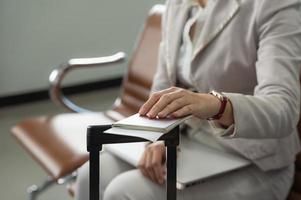 Passagère tenant un passeport avec un billet et un ordinateur portable avec une autre main alors qu'elle était assise au terminal de l'aéroport photo