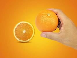 main tenant des fruits orange et des tranches d'orange sur fond orange photo