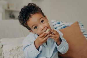 mignon garçon mulâtre aux grands yeux noisette mangeant des bonbons à la maison photo