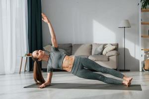 sur le tapis. jeune femme au corps mince et en vêtements de yoga est à la maison photo