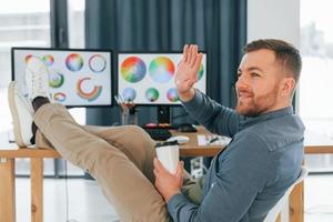 assis sur la chaise, détendu. designer masculin travaillant au bureau à l'aide d'un ordinateur photo