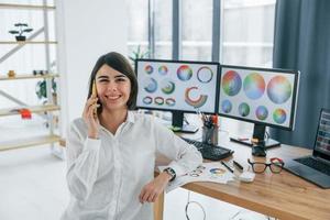 parler au téléphone. femme designer travaillant au bureau à l'aide d'un ordinateur photo