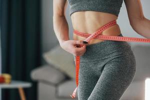 ruban à mesurer de couleur rose autour de la taille. jeune femme au corps mince et en vêtements de yoga est à la maison photo