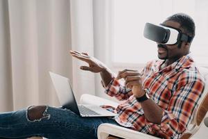 homme afro-américain dans des lunettes de réalité virtuelle voir l'achat en ligne sur un ordinateur portable. technologie, commerce électronique photo