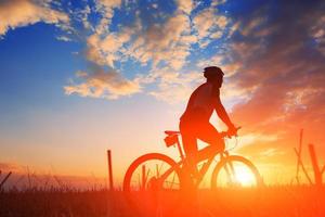 silhouette d'un motard et vélo sur fond de coucher de soleil. photo