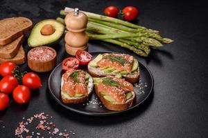 sandwich toast au beurre, avocat et saumon, décoré de roquette et de graines de sésame, sur fond de pierre noire photo