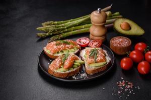 sandwich toast au beurre, avocat et saumon, décoré de roquette et de graines de sésame, sur fond de pierre noire photo