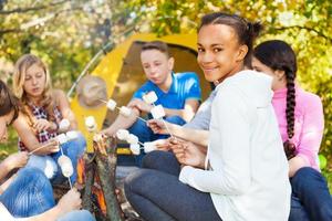 adolescents avec des bâtons de guimauve assis près d'un feu de joie