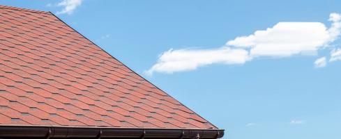 nouveau toit avec des bardeaux rouges contre le ciel bleu. tuiles sur le toit de la maison. utiliser pour annoncer la fabrication et l'entretien du toit. texture tachetée. toiture abordable. bannière avec espace de copie. photo