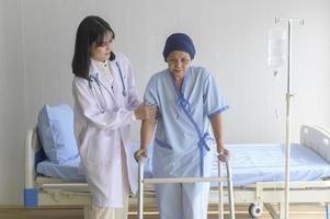 médecin aidant une patiente cancéreuse portant un foulard avec une marchette à l'hôpital, des soins de santé et un concept médical photo