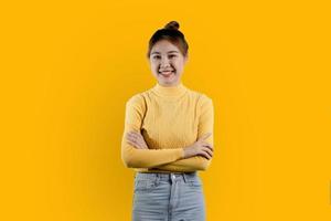 portrait d'une belle femme asiatique dans une chemise jaune debout avec les bras croisés et souriant. concept de portrait utilisé pour la publicité et la signalisation, isolé sur fond jaune, espace de copie. photo