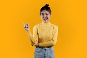 portrait d'une belle femme asiatique dans une chemise jaune debout et pointant. concept de portrait utilisé pour la publicité et la signalisation, isolé sur fond blanc, espace de copie. photo