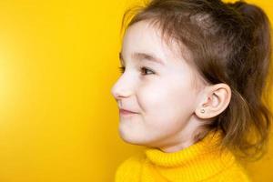 perçage d'oreille chez un enfant - une fille montre une boucle d'oreille dans son oreille faite d'un alliage médical. fond jaune, portrait d'une jeune fille de profil. photo