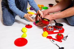 papa et sa fille jouent avec des légumes et des fruits en plastique tranchés avec du velcro, cuisinent des aliments sur un réchaud à jouets dans un bol. la cuisine des enfants, une fille apprend à cuisiner. fond blanc, gros plan. fête des pères photo