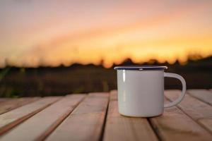 tasse à café sur la table en bois avec le fond du lever du soleil. mise au point douce. photo