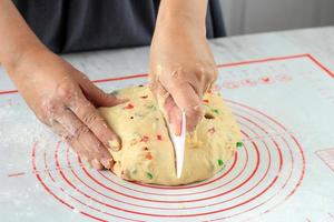 la main du boulanger coupe la pâte à pain aux fruits de levure crue sur fond de tableau blanc avec un couteau en plastique.
